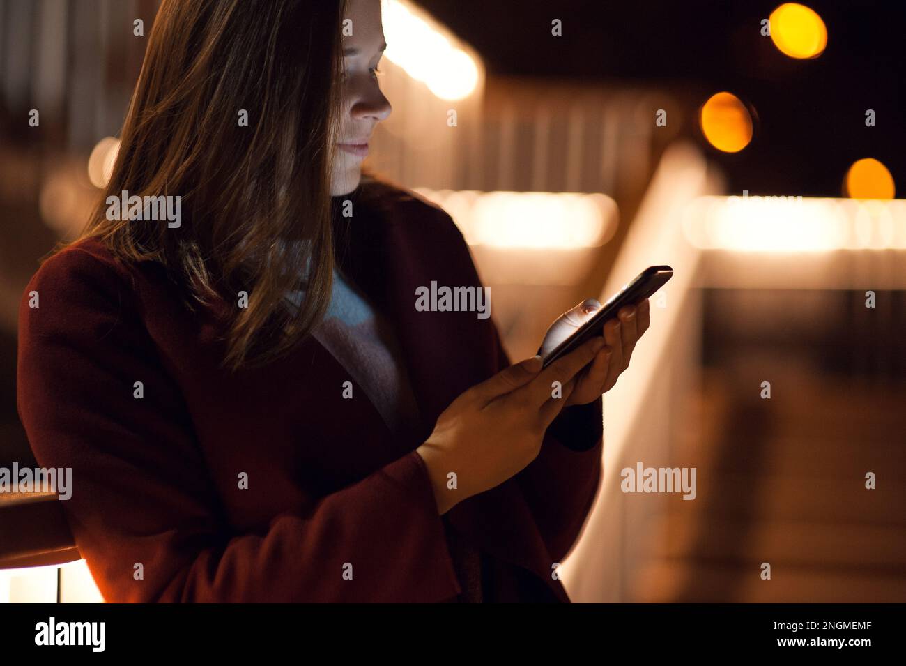 Primo piano donna urbana felice e sorridente che usa uno smartphone moderno nel quartiere del centro, contro gli edifici illuminati della città Foto Stock