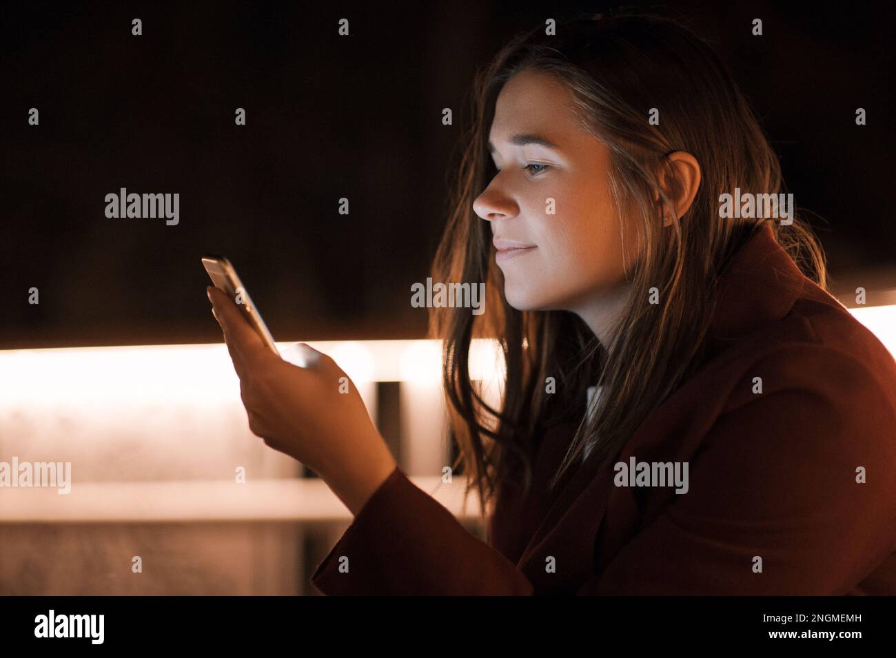 Primo piano donna urbana felice e sorridente che usa uno smartphone moderno nel quartiere del centro, contro gli edifici illuminati della città Foto Stock
