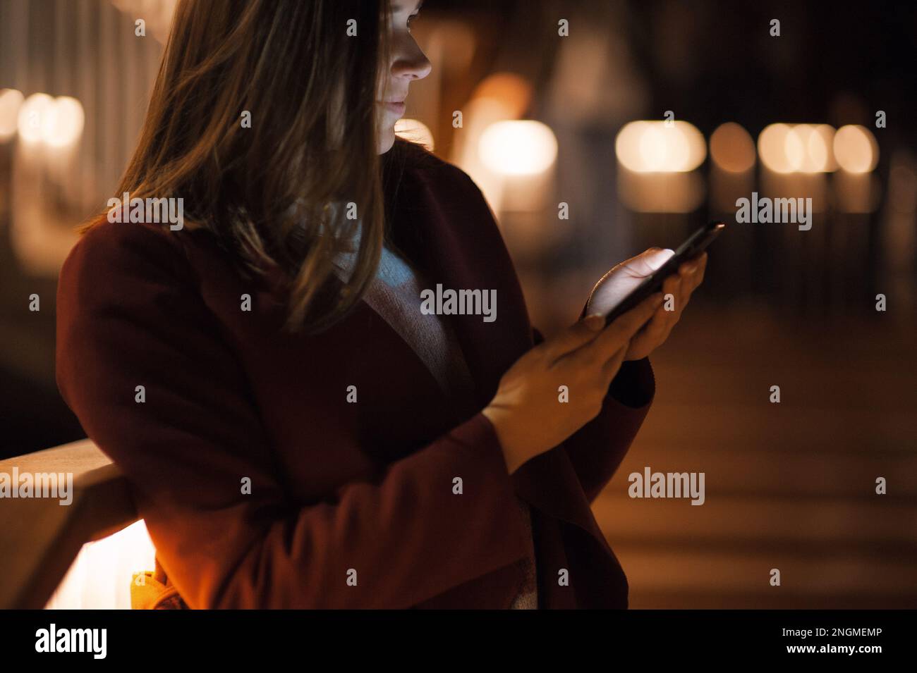 Primo piano donna urbana felice e sorridente che usa uno smartphone moderno nel quartiere del centro, contro gli edifici illuminati della città Foto Stock
