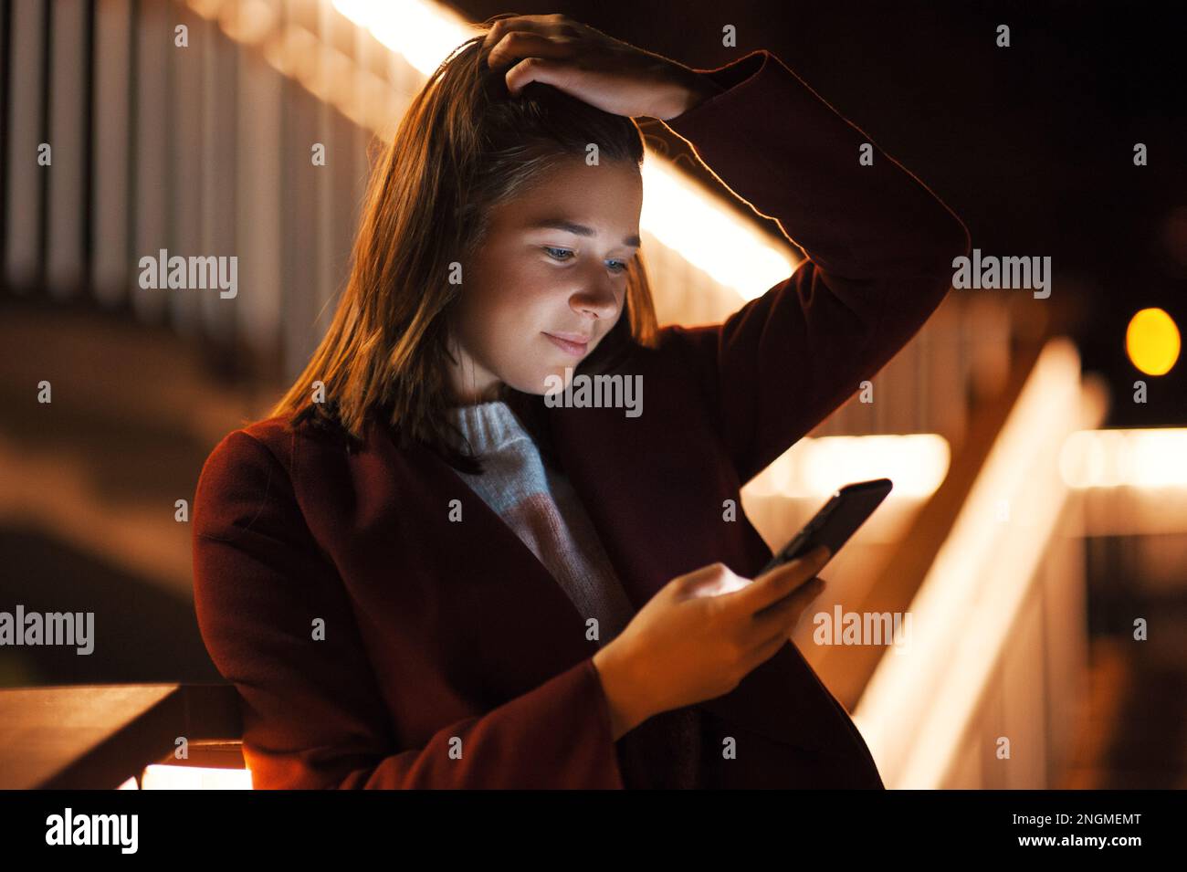 Primo piano donna urbana felice e sorridente che usa uno smartphone moderno nel quartiere del centro, contro gli edifici illuminati della città Foto Stock