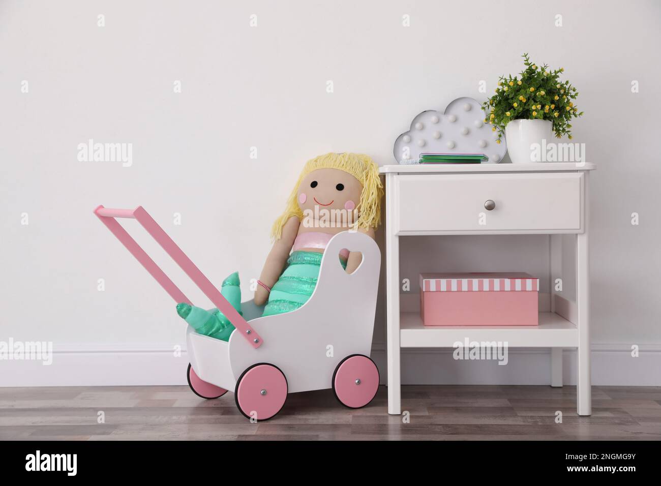 Passeggino giocattolo con bambola e supporto vicino alla parete della luce nella stanza del bambino. Design degli interni Foto Stock
