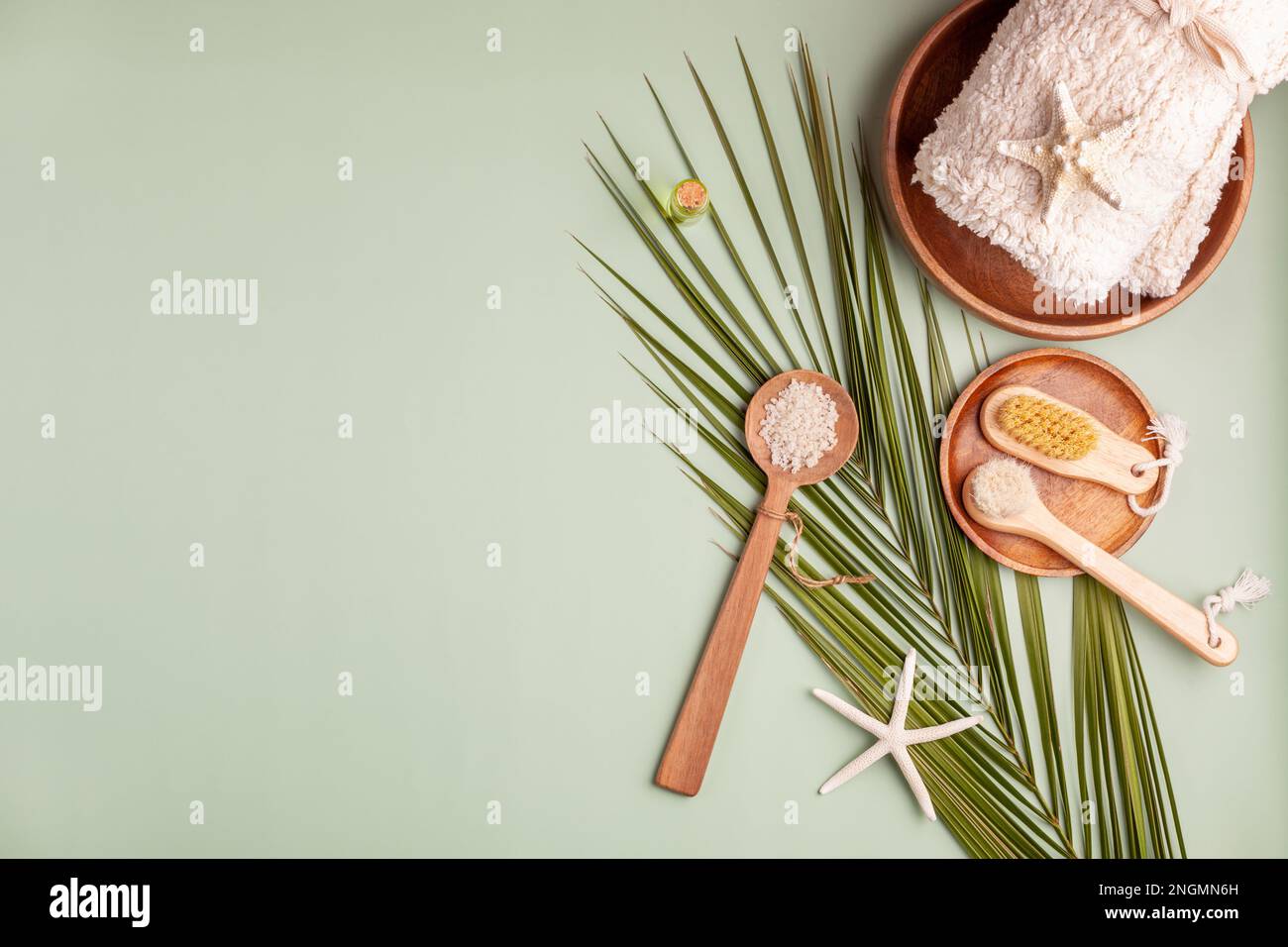 composizione spa con foglie di palma, asciugamano, sale marino e stelle marine, fondo verde chiaro, vista dall'alto Foto Stock