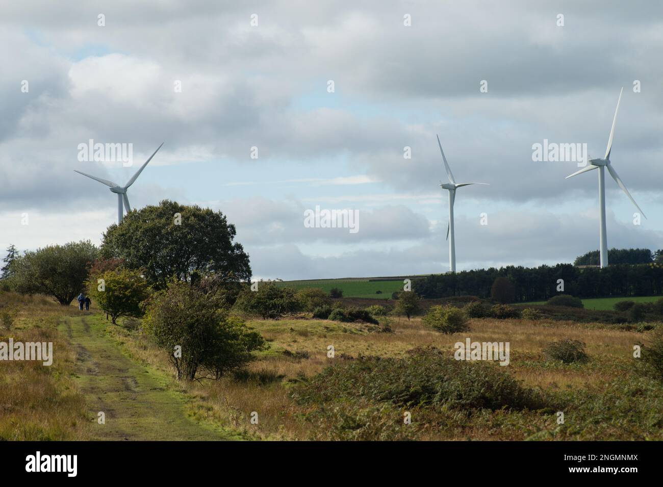 Una famiglia che cammina attraverso il terreno edificabile con terreni agricoli in lontananza e turbine eoliche lontane Foto Stock