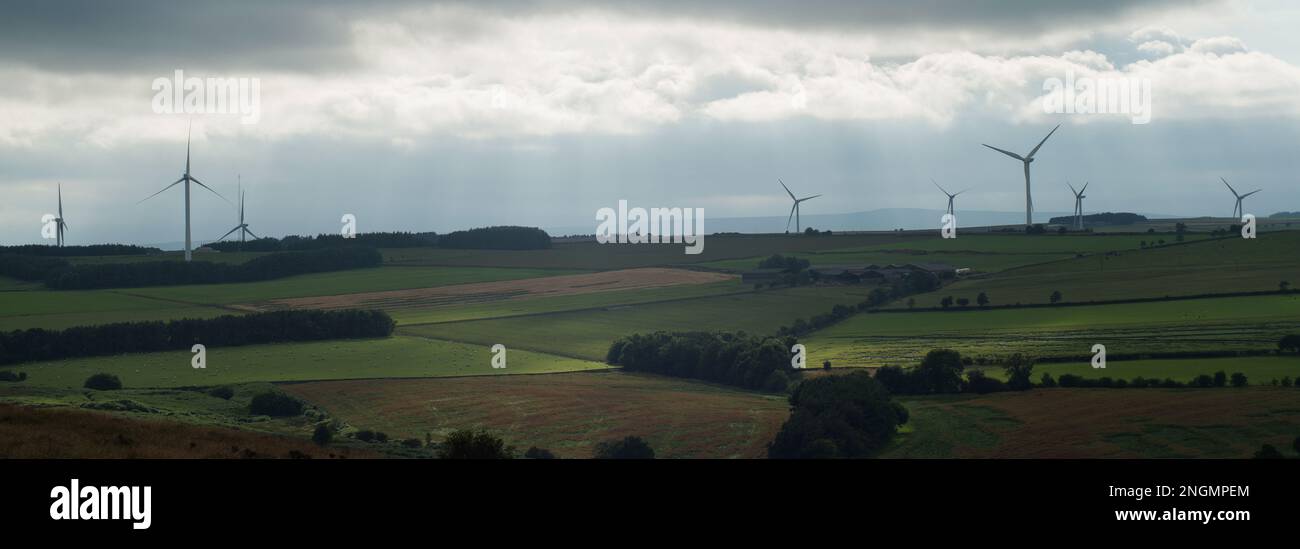 Paesaggio che mostra aree luminose di luce solare che si infrangono attraverso le nuvole con turbine eoliche in lontananza Foto Stock