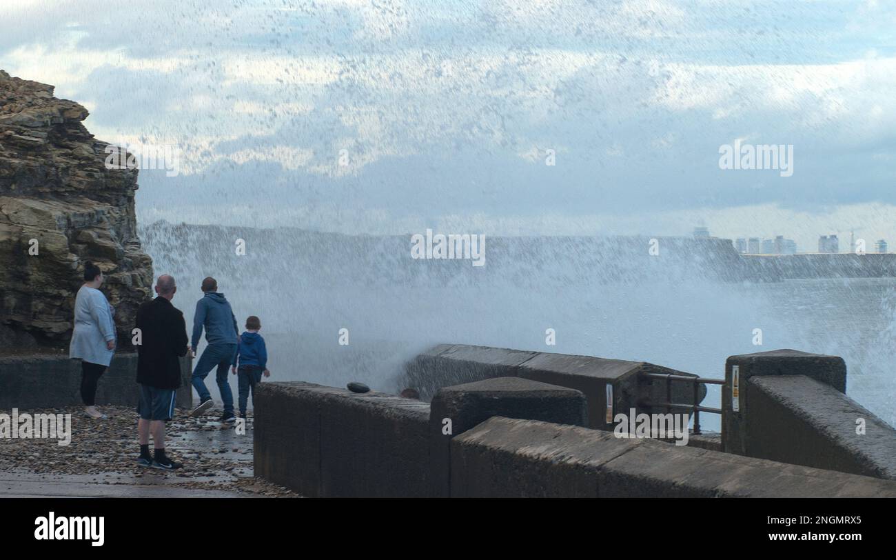 Il gruppo di persone si prende la copertura mentre i mari pesanti si schiantano sul lungomare gettando enormi colonne di spruzzi di mare Foto Stock