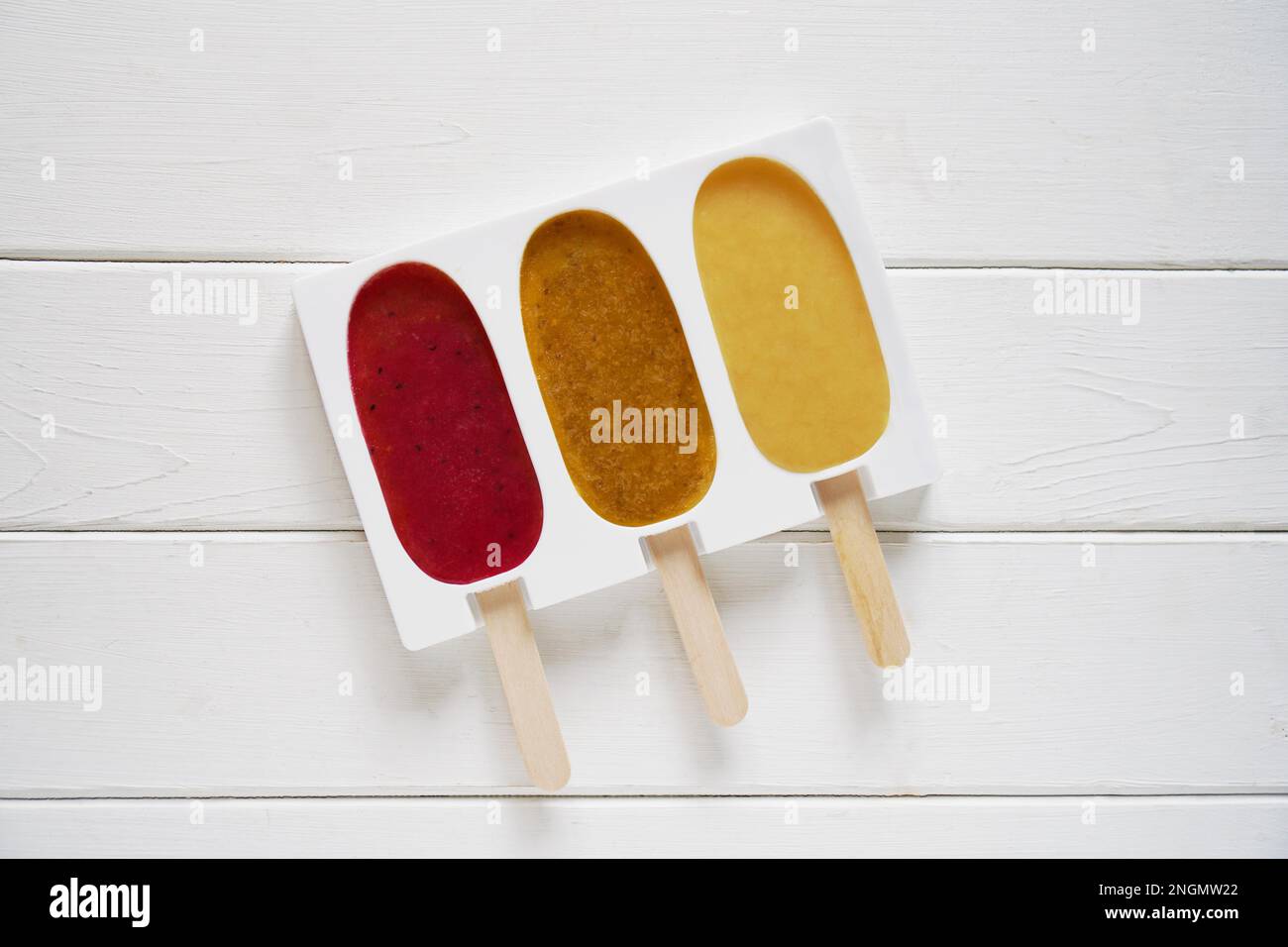 tre diversi frullato di frutta popsicle in silicone riutilizzabile forma pop ghiaccio o su sfondo di legno bianco - facendo fragola, frutto della passione e. Foto Stock