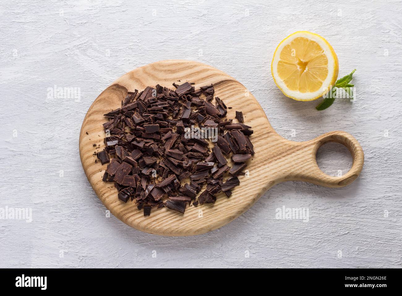 Asse di legno con cioccolato amaro tritato, mezzo limone e menta su sfondo grigio chiaro testurizzato, vista dall'alto, piatto Foto Stock