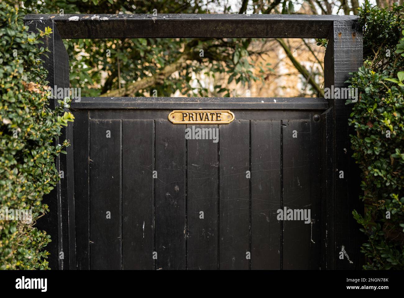Fuoco poco profondo di un ottone ornato segno privato visto su un cancello di legno che conduce ad un giardino privato. Foto Stock