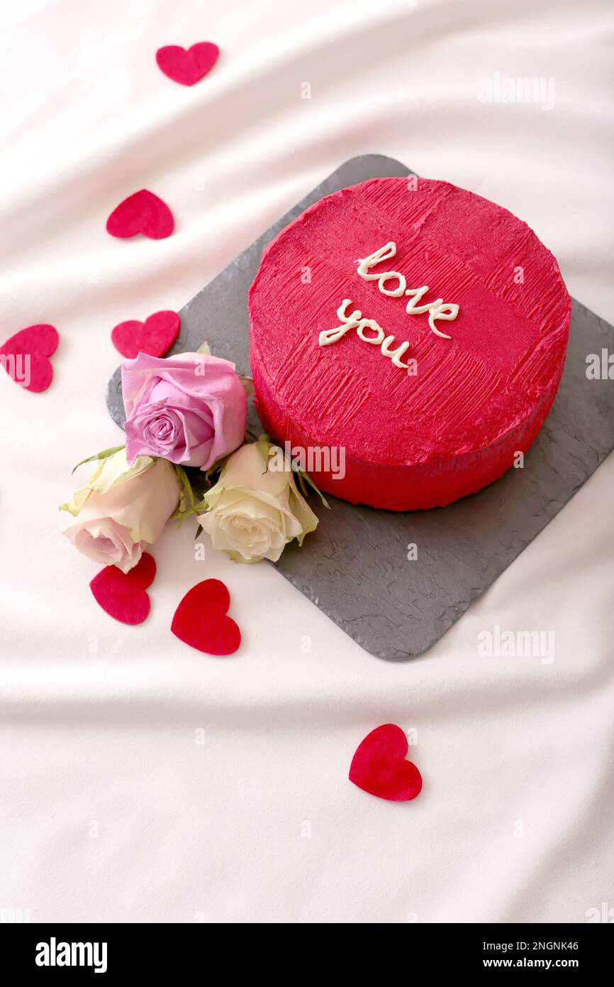 gustosa torta bento rossa e rose giacciono sul letto bianco Foto Stock