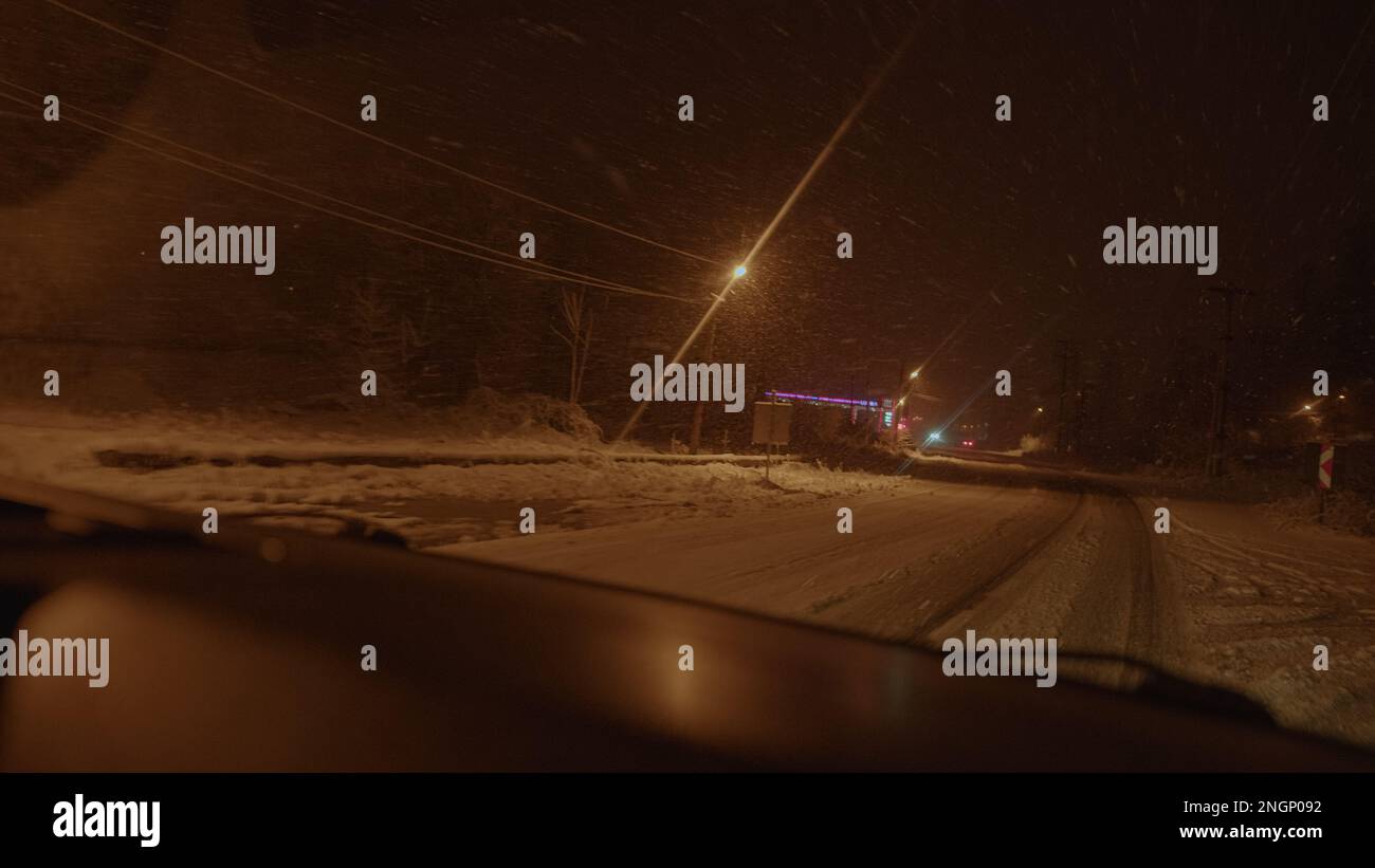 Guida attraverso un Winter Wonderland: Scene di neve sfocata e scintillanti luci di Bokeh riflesse su un finestrino anteriore dell'automobile di notte, ideale per Urban Lifest Foto Stock