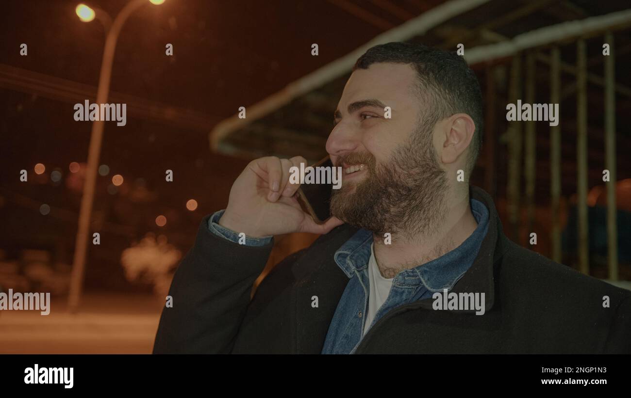 Chiamata telefonica: Sorridente, Bearded, Tall Young Man che risponde alla chiamata in arrivo in scenario invernale Foto Stock