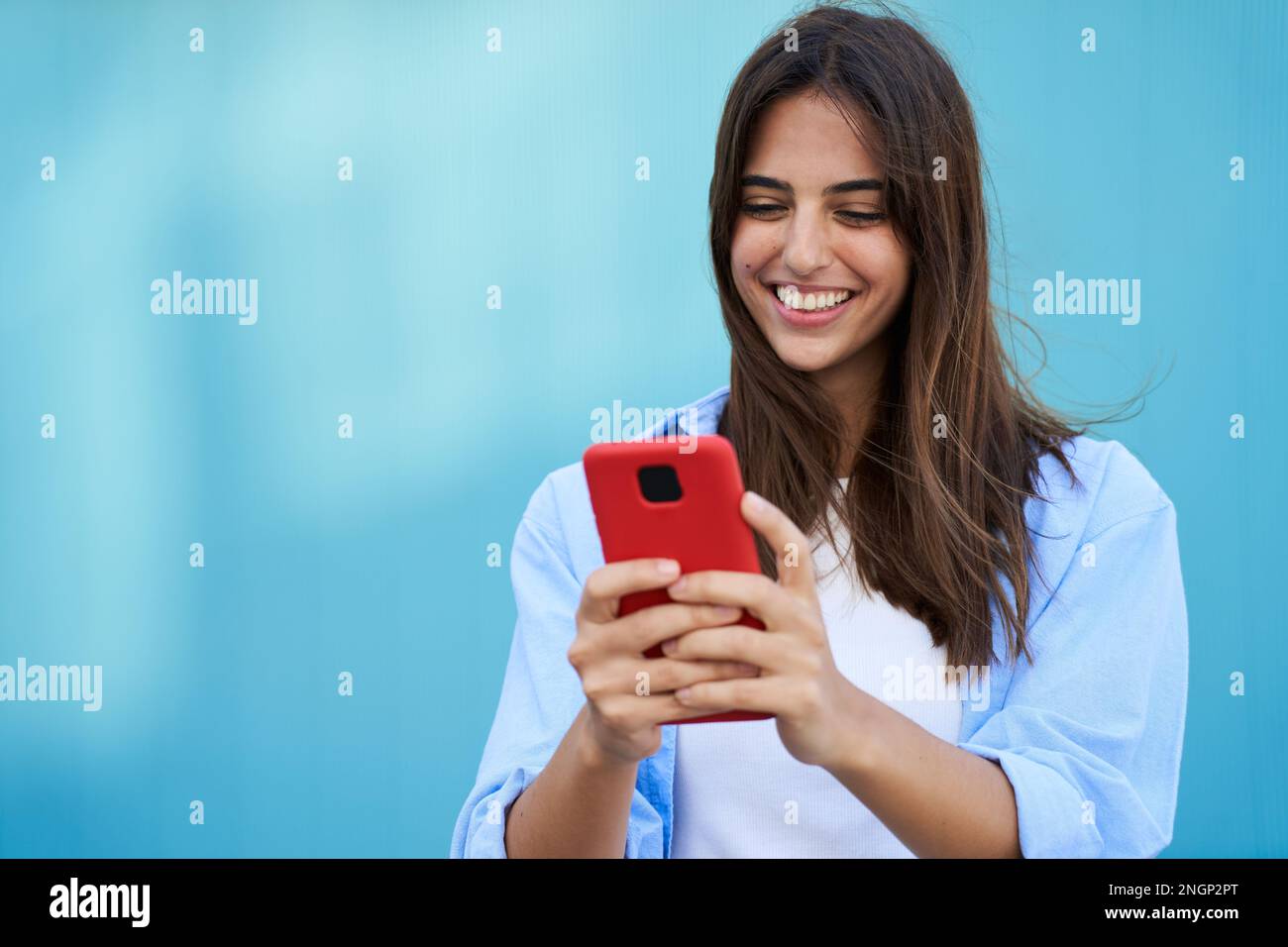 Una giovane ragazza che usa un telefono cellulare con uno sfondo blu. Una donna sorridente che flirta attraverso un'app. Foto Stock
