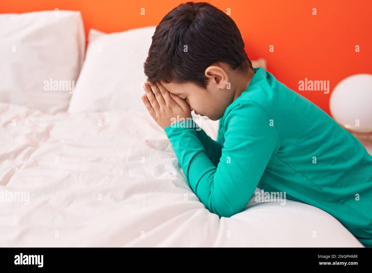 Adorabile ragazzo ispanico seduto sul pavimento in preghiera in camera da letto Foto Stock