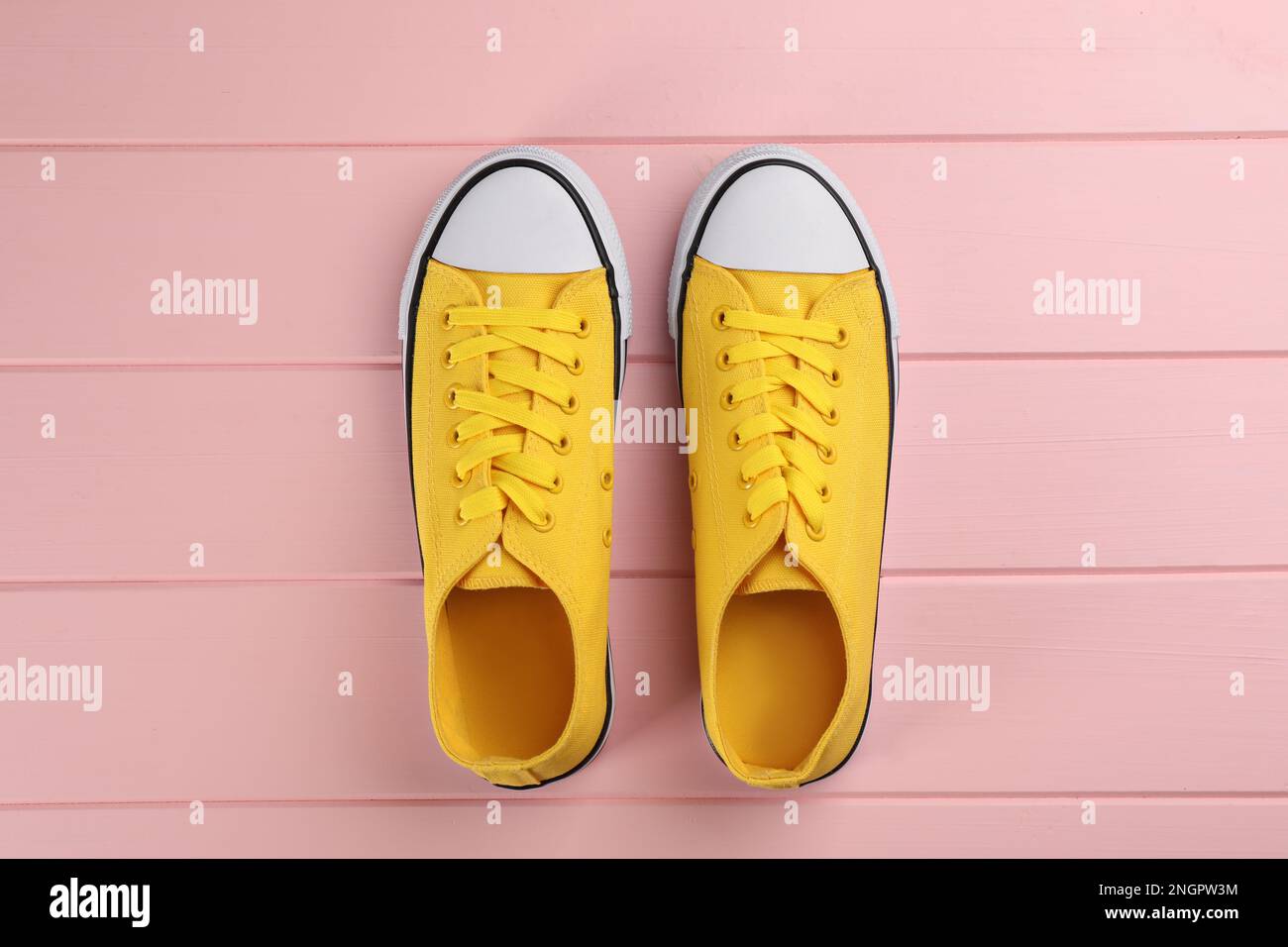 Paio di sneaker gialle su tavolo in legno rosa, a posa piatta Foto Stock