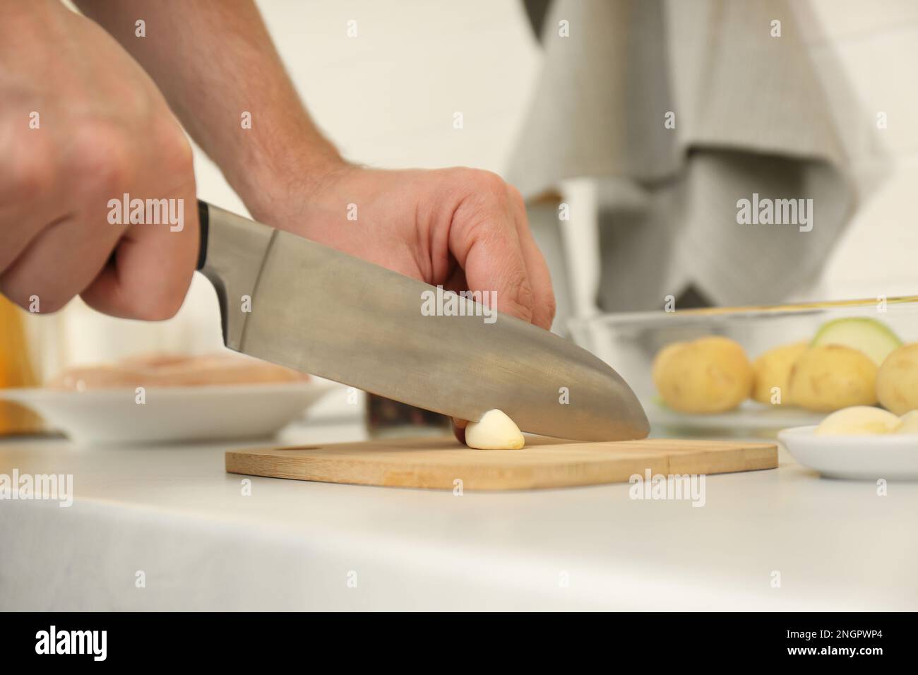 Uomo che taglia l'aglio a tavola in cucina, spicchio Foto Stock