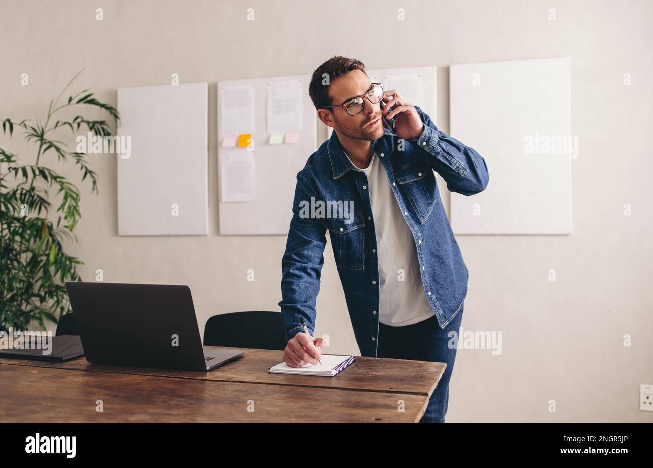 Un uomo d'affari attento che scrive appunti durante una telefonata con i suoi clienti. Giovane uomo d'affari che fa progetti al telefono. un uomo d'affari con gli occhiali funziona Foto Stock