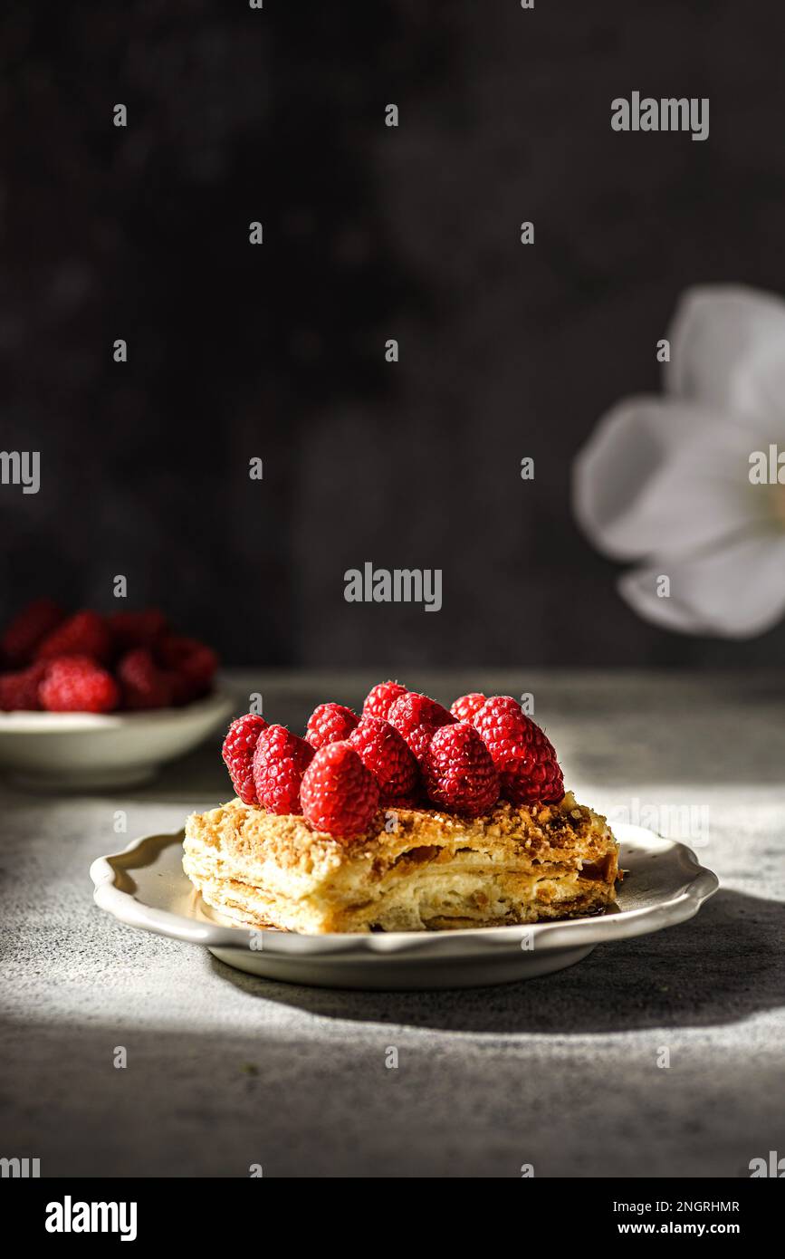 torta napoleone su sfondo grigio. la torta è fatta di dolci di pasta sfoglia con crema pasticcera e decorata con lamponi freschi Foto Stock