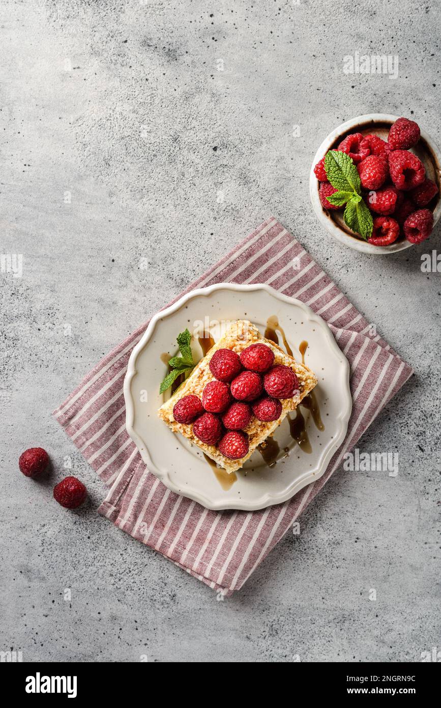 torta napoleone su sfondo grigio. la torta è fatta di dolci di pasta sfoglia con crema pasticcera e decorata con lamponi freschi Foto Stock