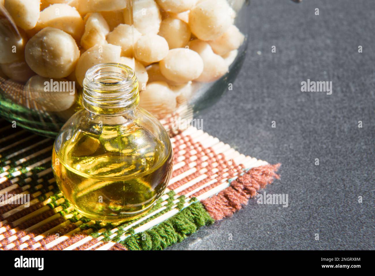 Ancora la vita con olio di Macadamia in bottiglia e noci nel vaso su sfondo grigio Foto Stock