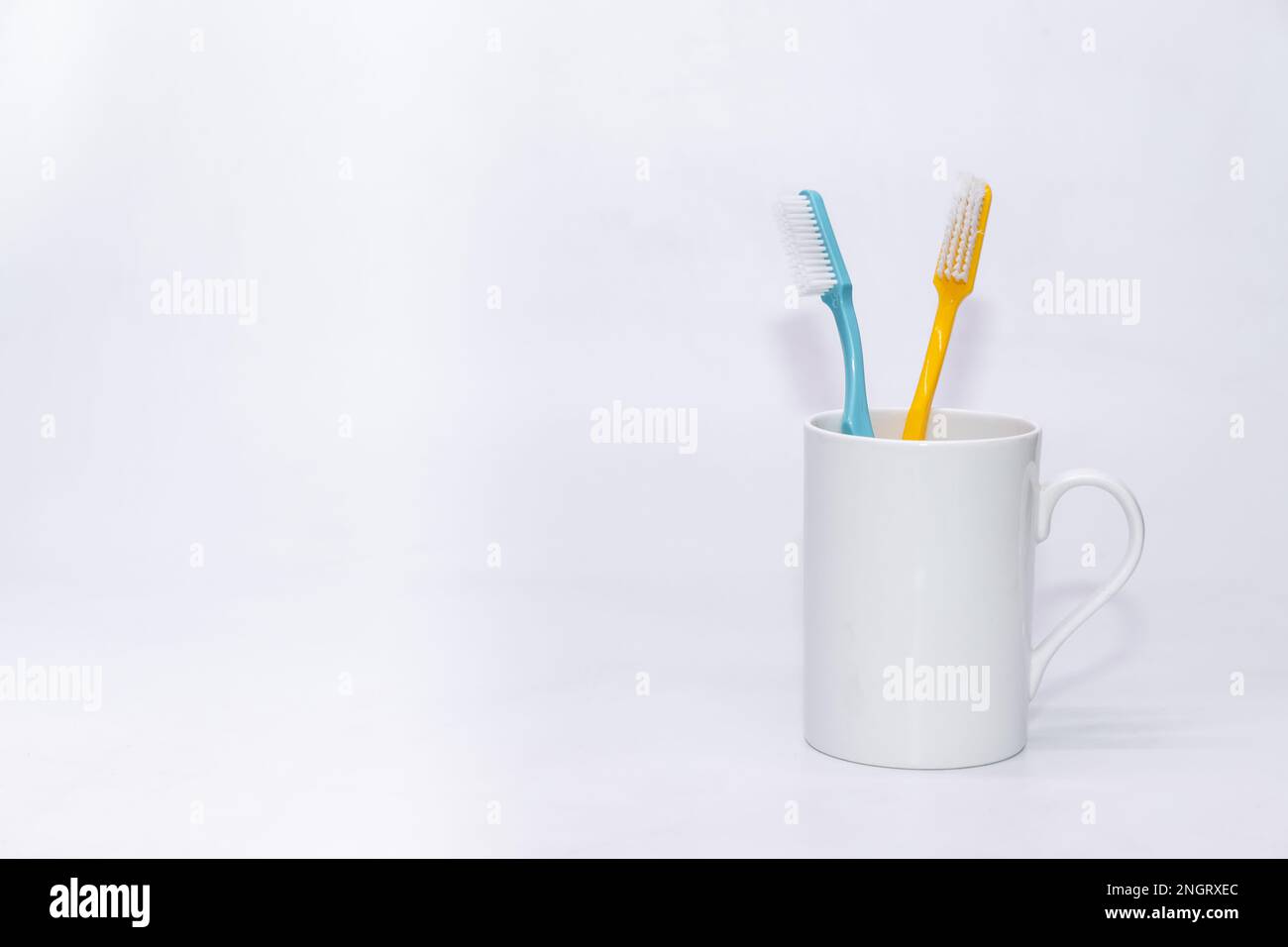Un paio di spazzolino da denti colorati tenuti all'interno di una tazza con sfondo bianco dello spazio di copia Foto Stock