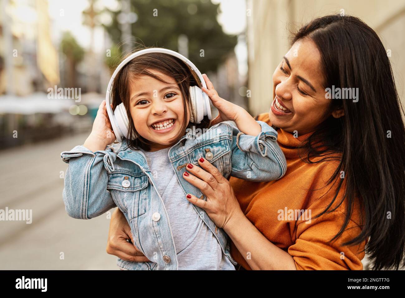 Felice madre filippina con sua figlia divertirsi ascoltando musica con le cuffie nel centro della città - concetto di amore per la famiglia Foto Stock
