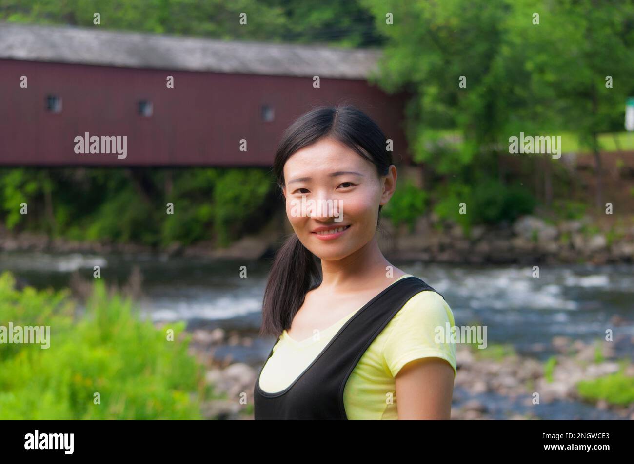 Una donna cinese felice con il ponte coperto cornovaglia occidentale sul fiume housatonic sullo sfondo. Foto Stock