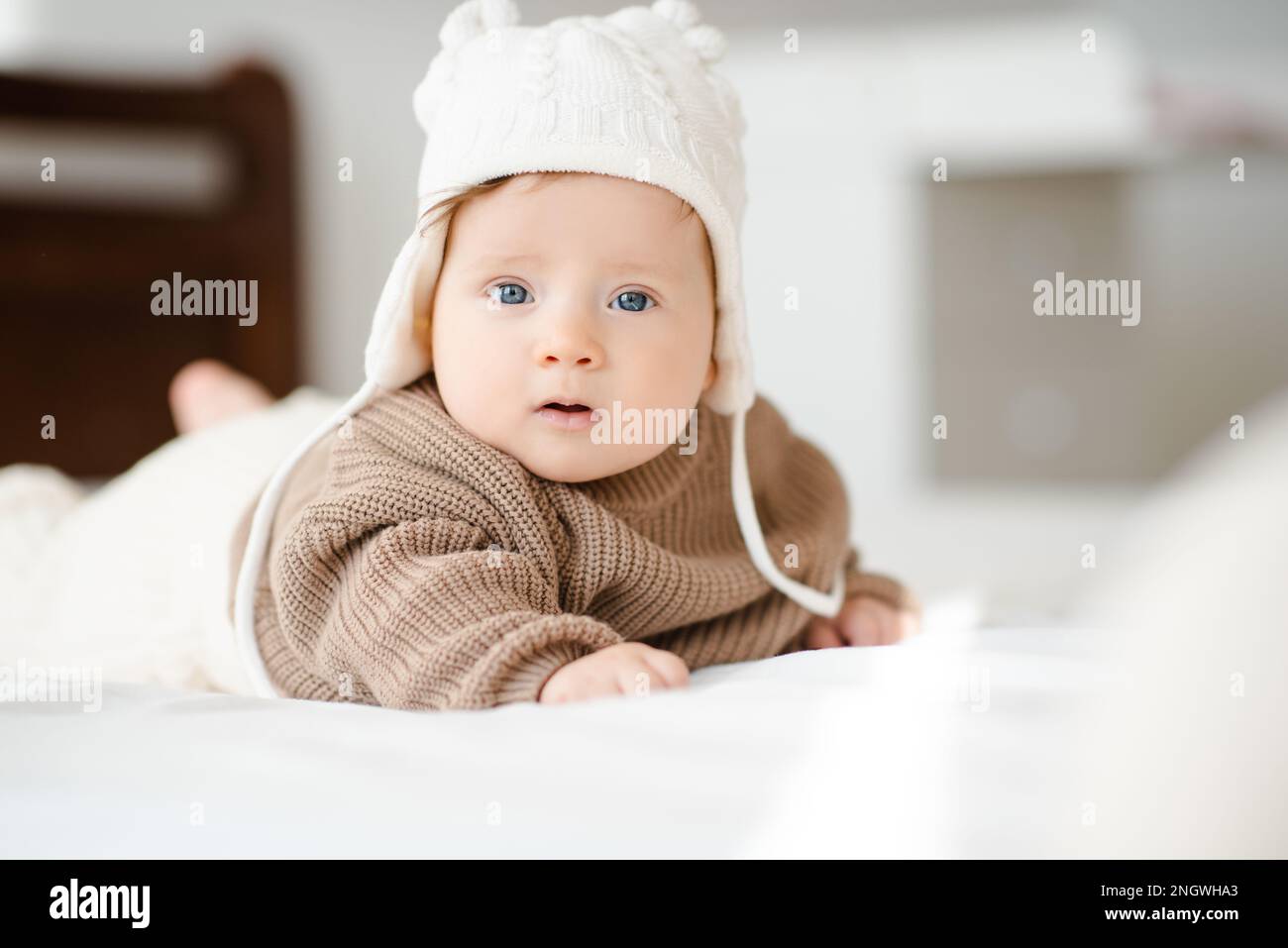 Carino bambino al di sotto di 1 anni indossare cappello a maglia e maglione che striscia nel letto guardando la macchina fotografica primo piano. Infanzia. Foto Stock