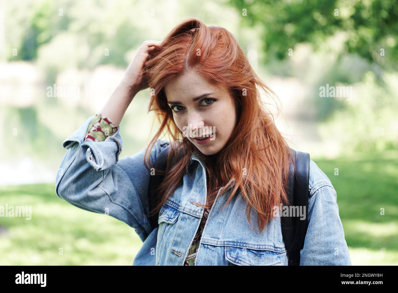Giovane donna indossando giacca denim giocando con i suoi capelli e dando un coy guardare - autentico persone reali all'aperto Foto Stock