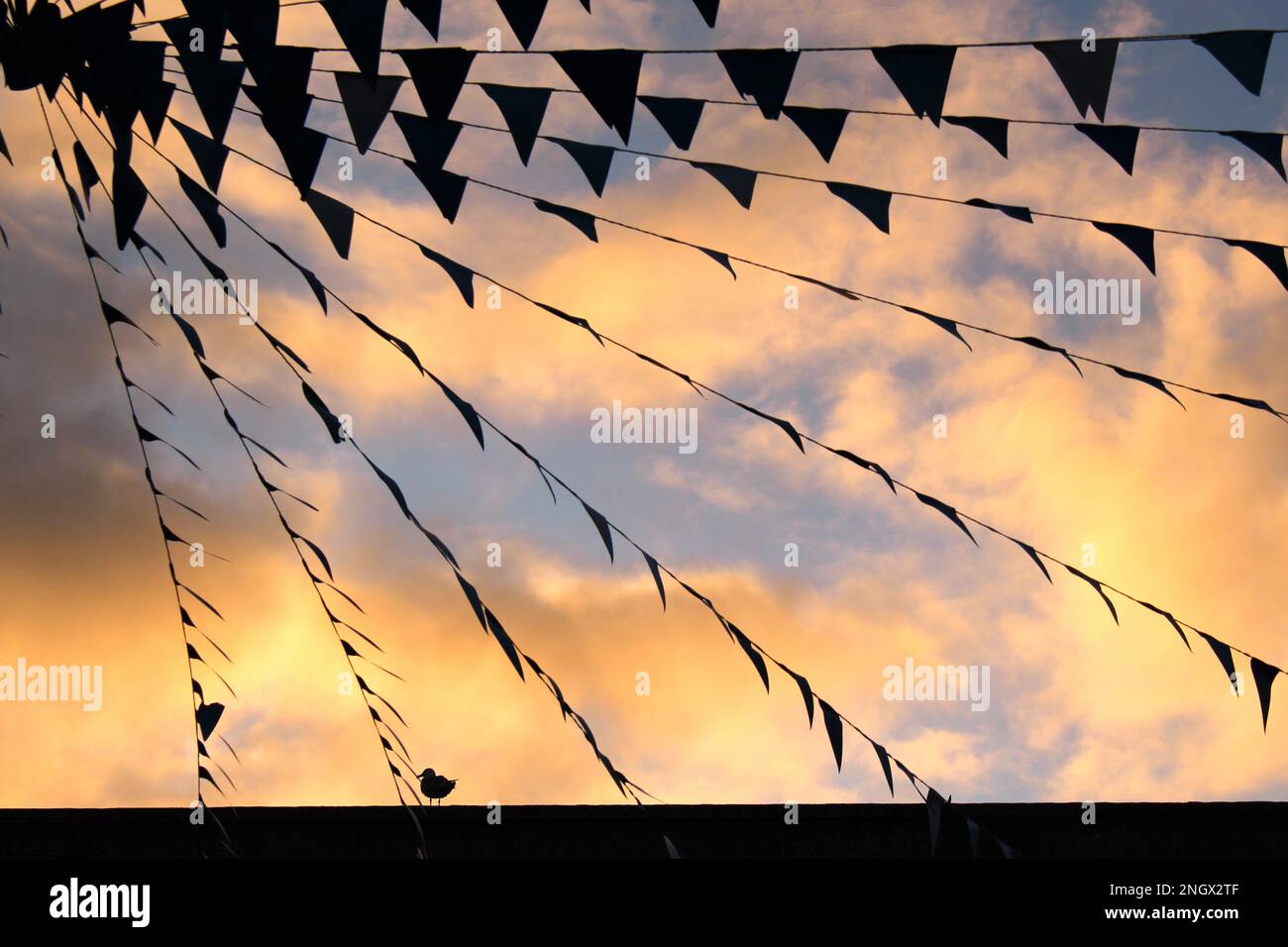 Silhouette di bandiere triangolari contro le nuvole di tramonto dorate ore sfondo con piccola silhouette di uccello sul fondo Foto Stock