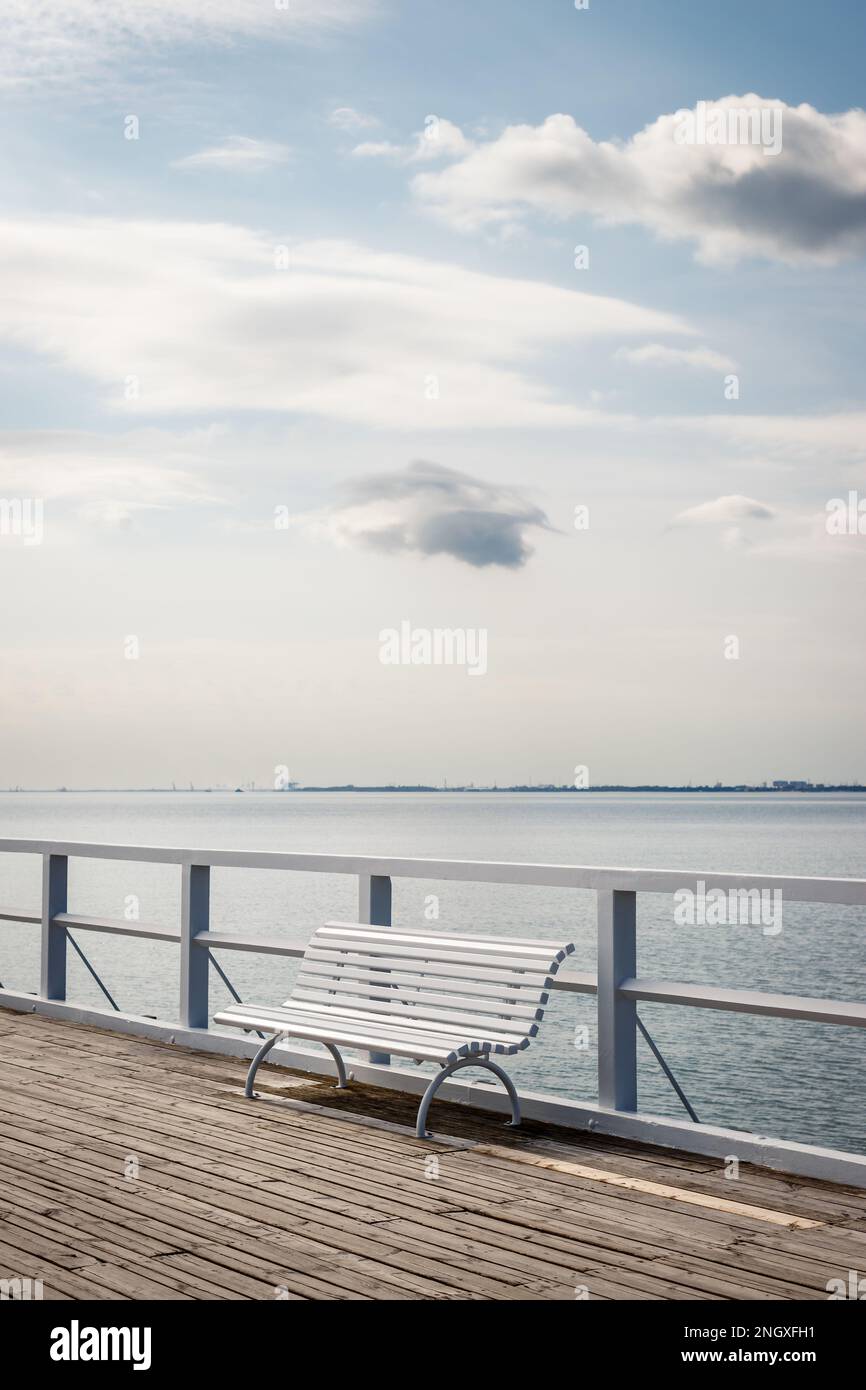 Panca bianca vuota sul molo della costa Mar Baltico. Paesaggio tranquillo con nuvole sul cielo Foto Stock