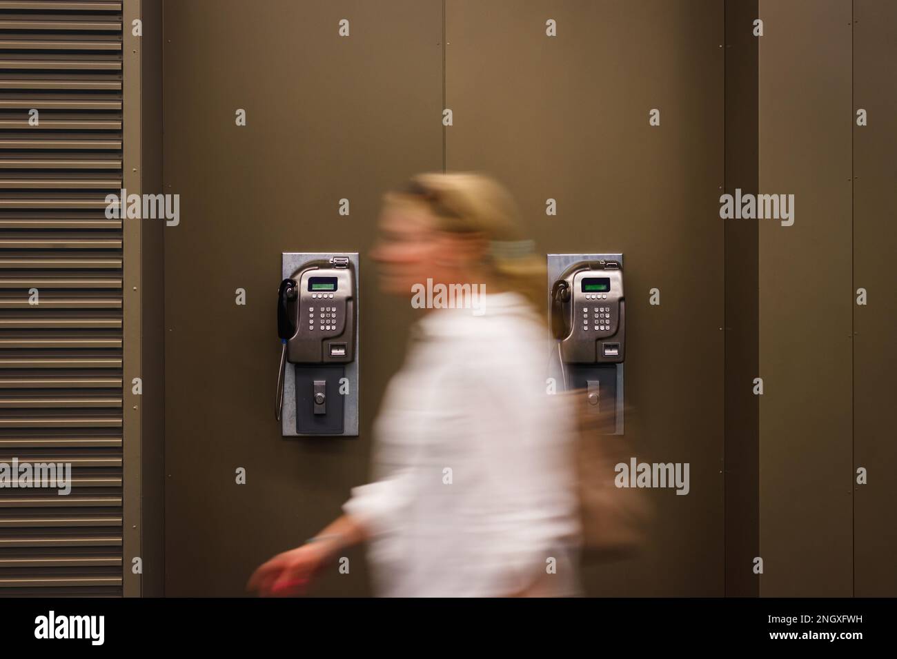 Donna in movimento sfocatura passando al telefono pubblico a gettoni a pagamento. Vecchio telefono sulla parete Foto Stock