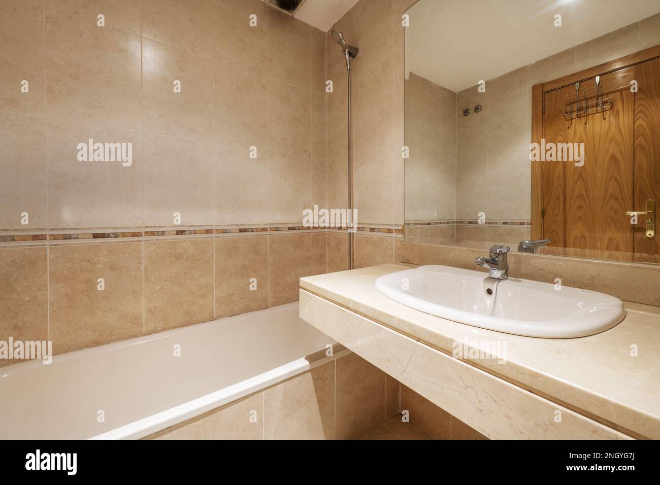 Bagno con lavabo in marmo crema senza armadio con specchio integrato nella parete e con una lunga vasca da bagno Foto Stock