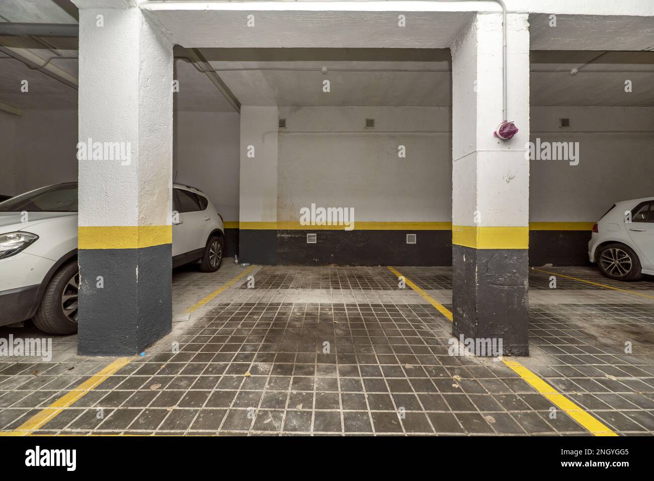 Posti auto delimitati con vernice gialla al piano terra di un edificio con garage e veicoli parcheggiati Foto Stock