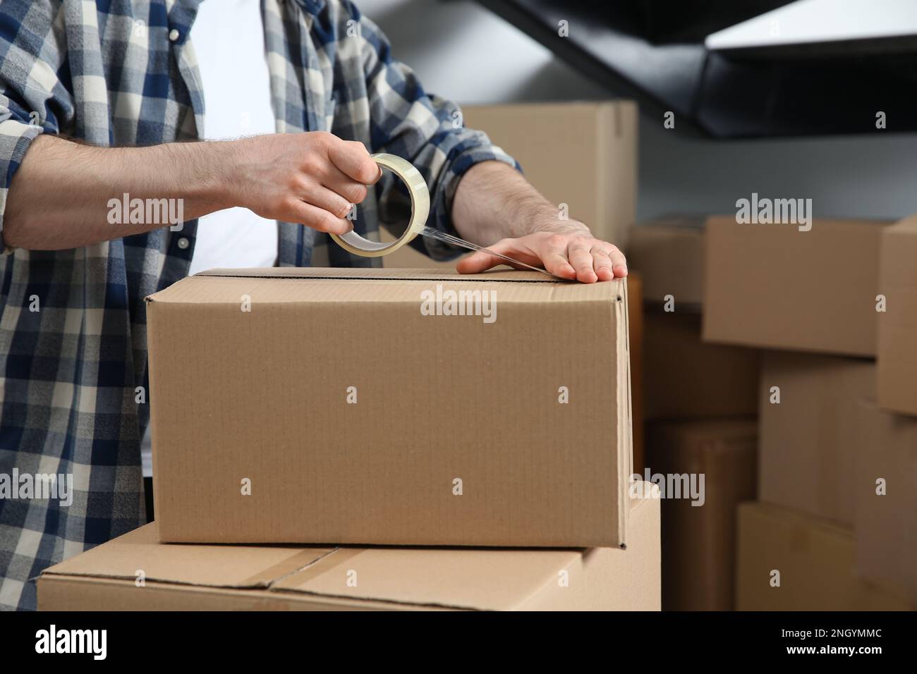 Uomo che nastrano scatola di cartone all'interno, primo piano. Giorno in movimento Foto Stock