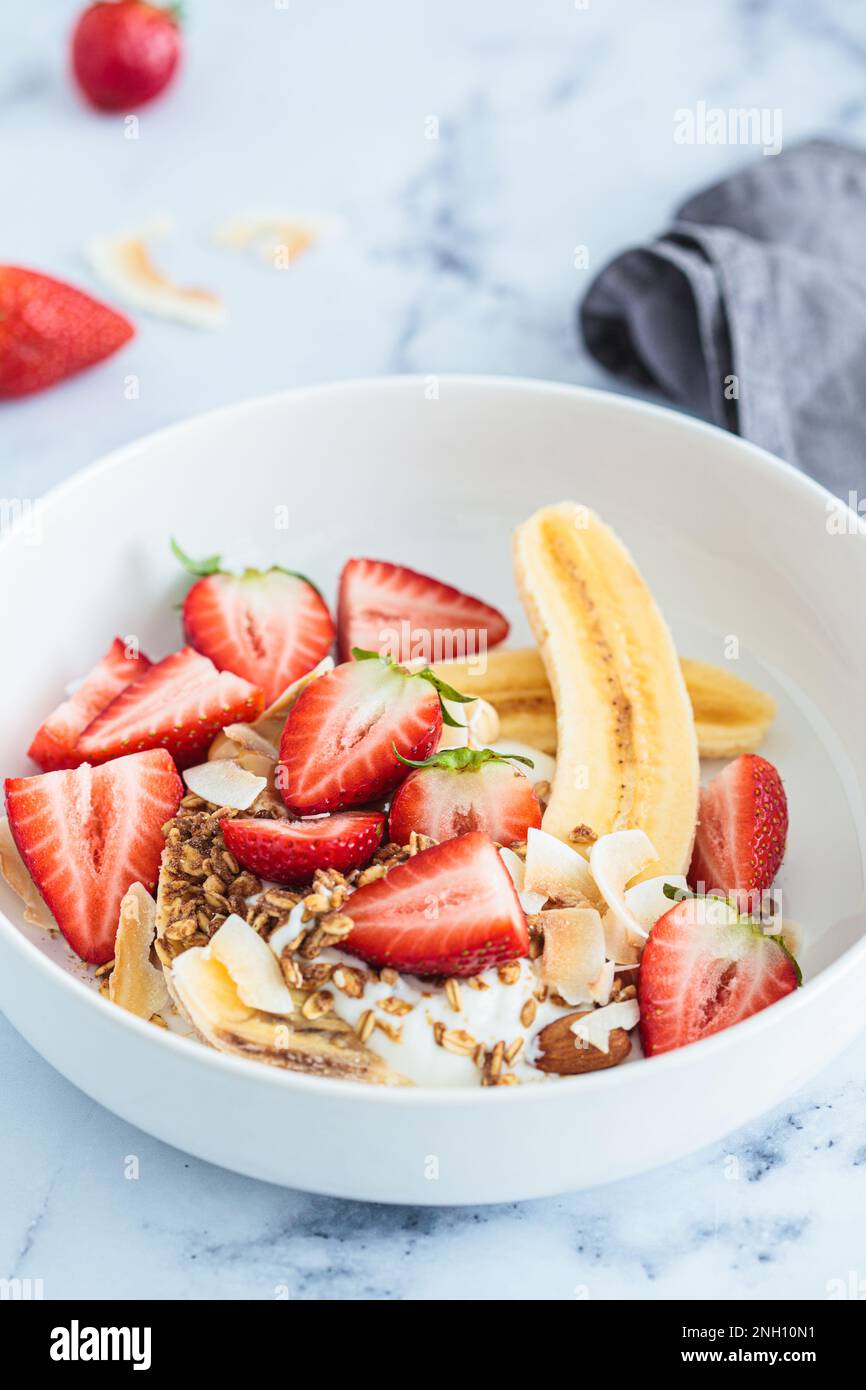 Ricetta sana di banana vegana con yogurt greco, fragole, muesli fatti in casa e burro di arachidi biologico. Foto Stock