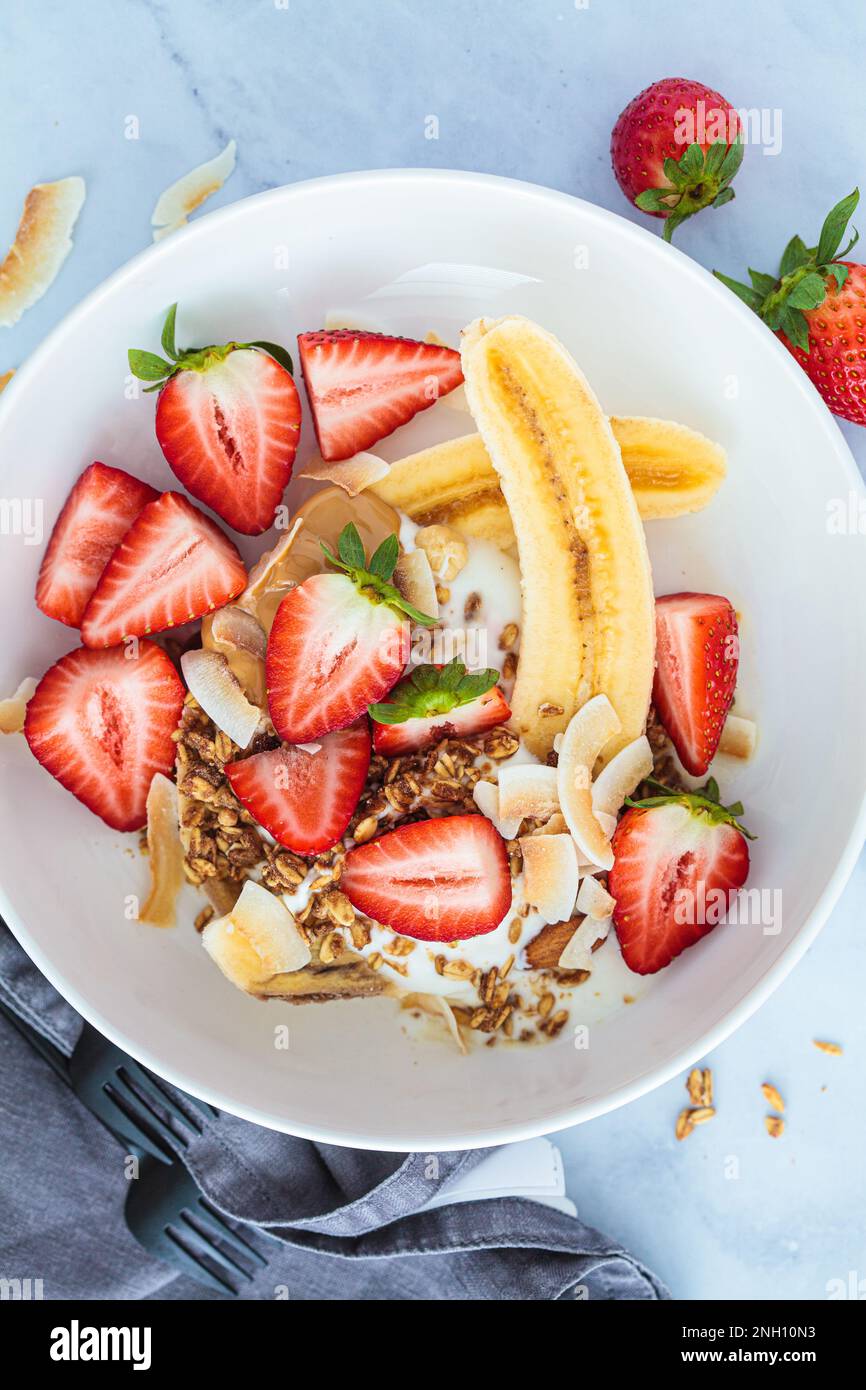Sana ricetta di banana vegana con yogurt greco, fragole, muesli fatti in casa e burro di arachidi biologico, vista dall'alto. Foto Stock