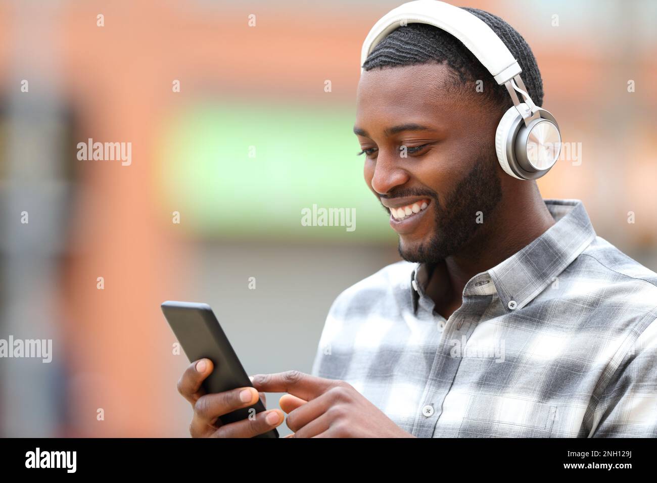 Uomo nero che ascolta musica controllare il telefono all'aperto in strada Foto Stock