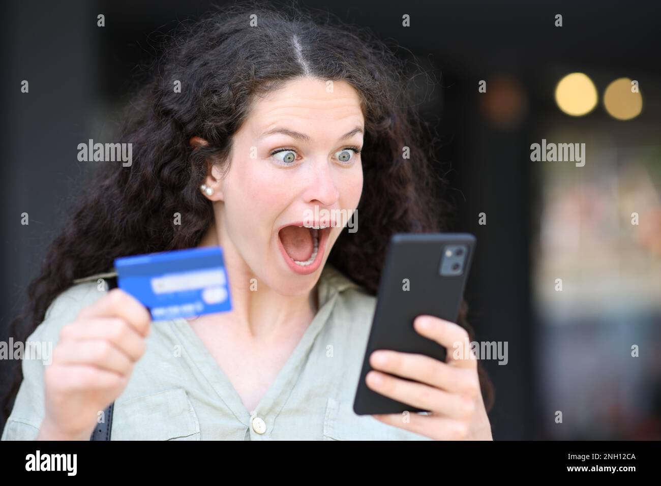 Donna sorpresa che acquista online con telefono e carta di credito Foto Stock