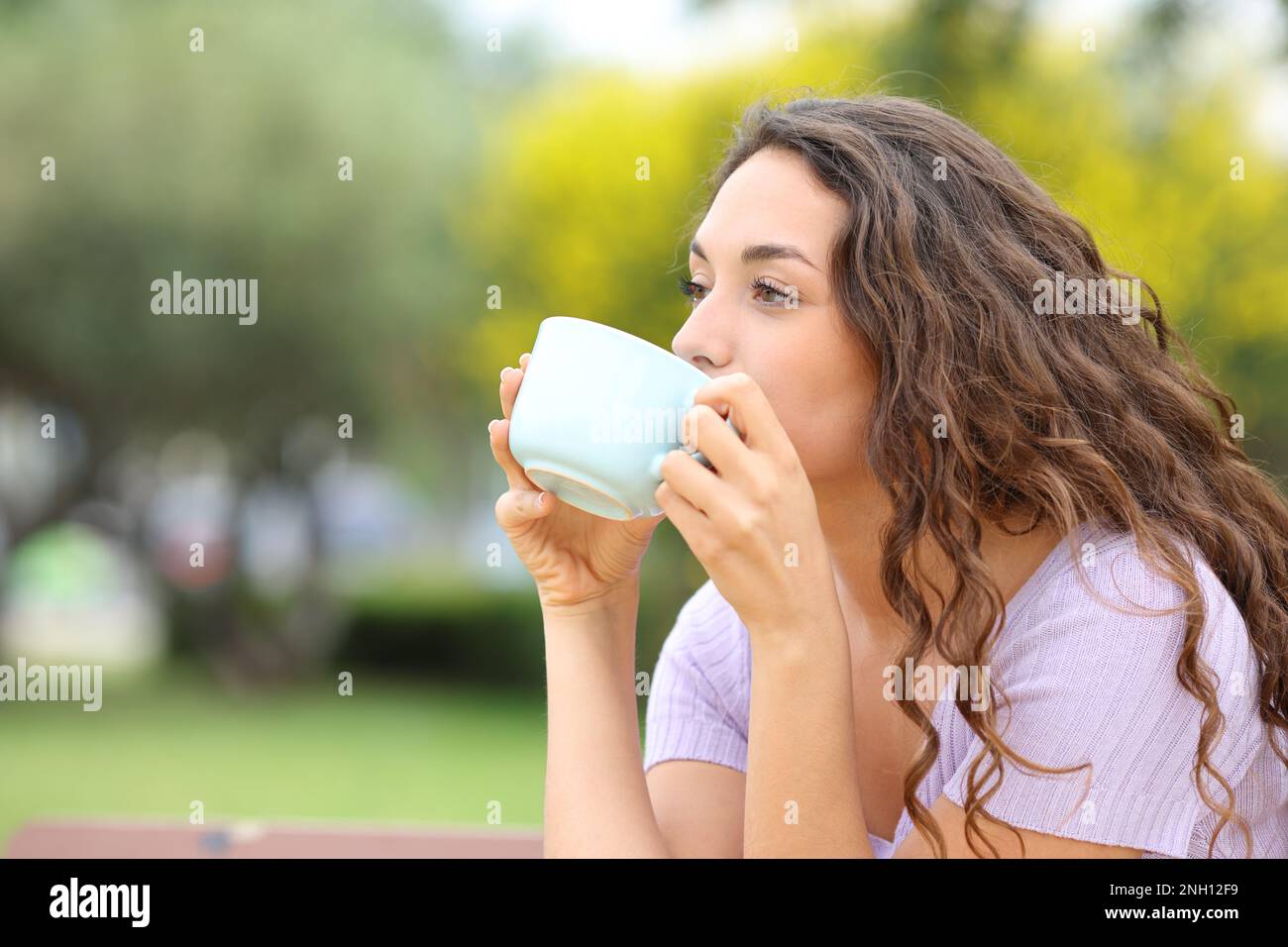 Donna che beve caffè seduto su una panca in un parco Foto Stock