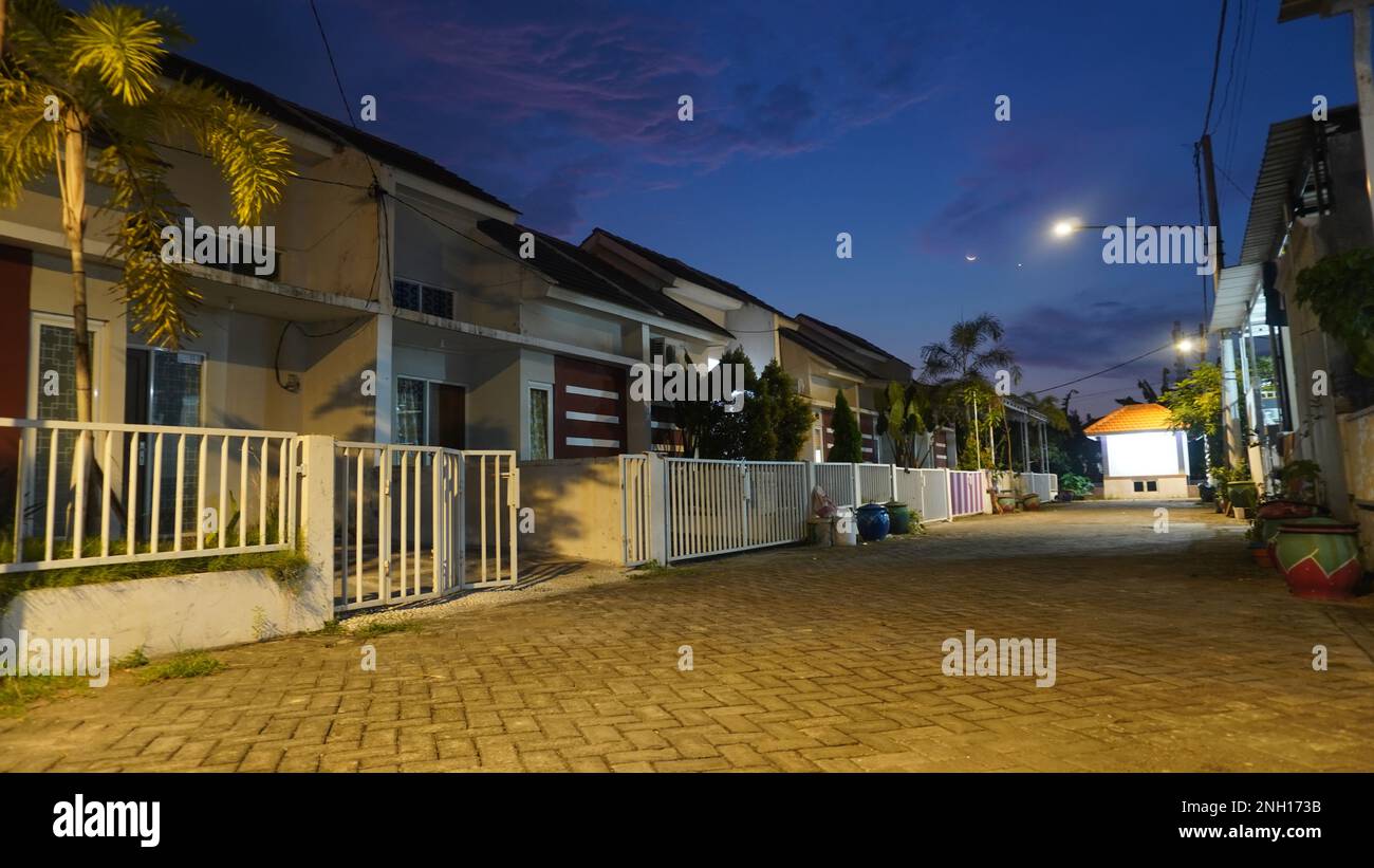 Notte scenario vuoto solitario e tranquilla strada di pavimentazione di casa residenziale a villaggio rurale con luna di Crescent Foto Stock