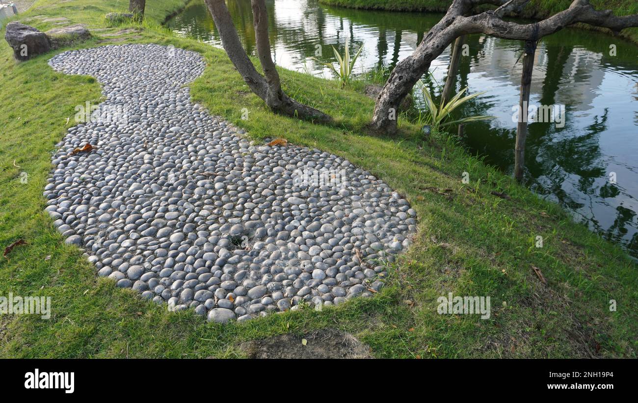 Pietre ordinate e organizzate vicino al laghetto del giardino possono essere utilizzate per la terapia di salute riflessologia del piede Foto Stock