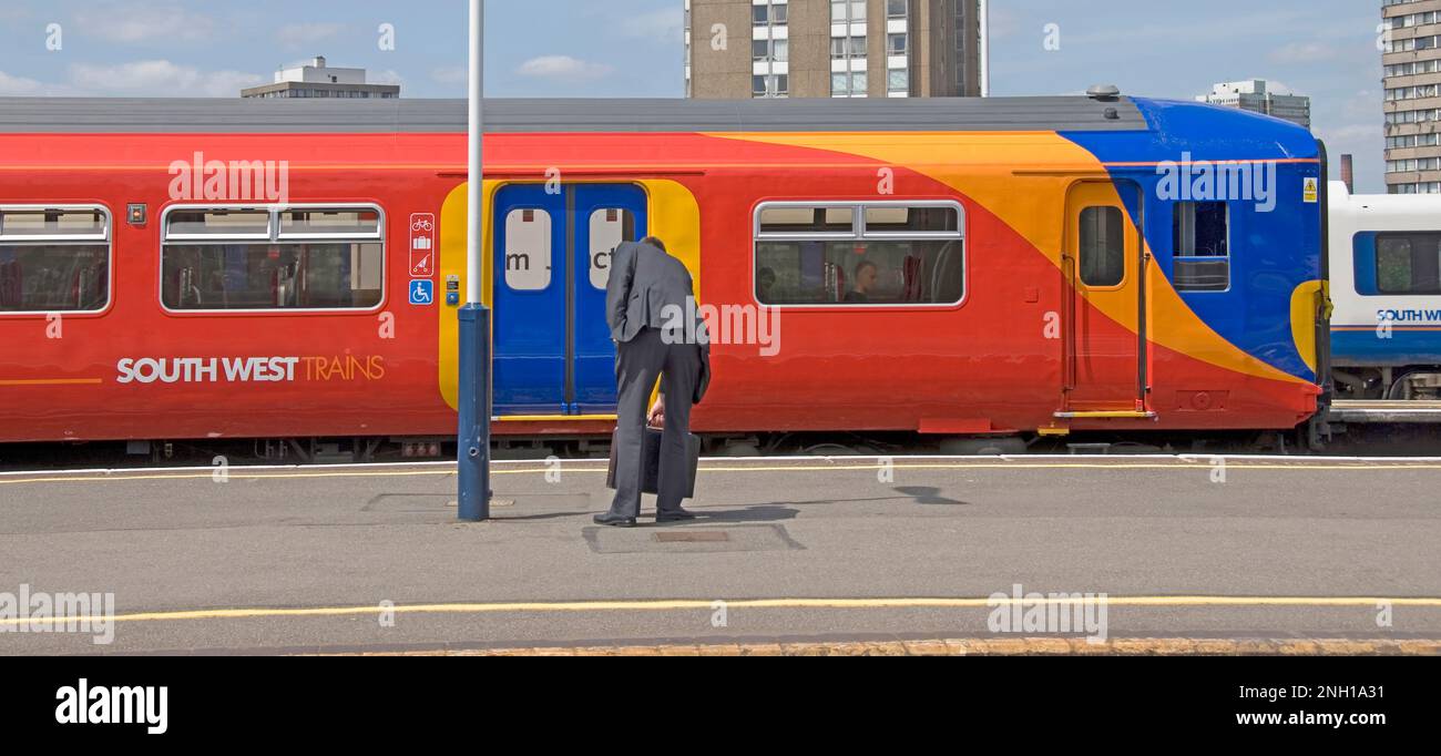 Clapham Junction stazione ferroviaria piattaforma di lavoro uomo d'affari in attesa sulla piattaforma raccoglie valigetta Sud Ovest treni servizio arriva per Londra UK Foto Stock