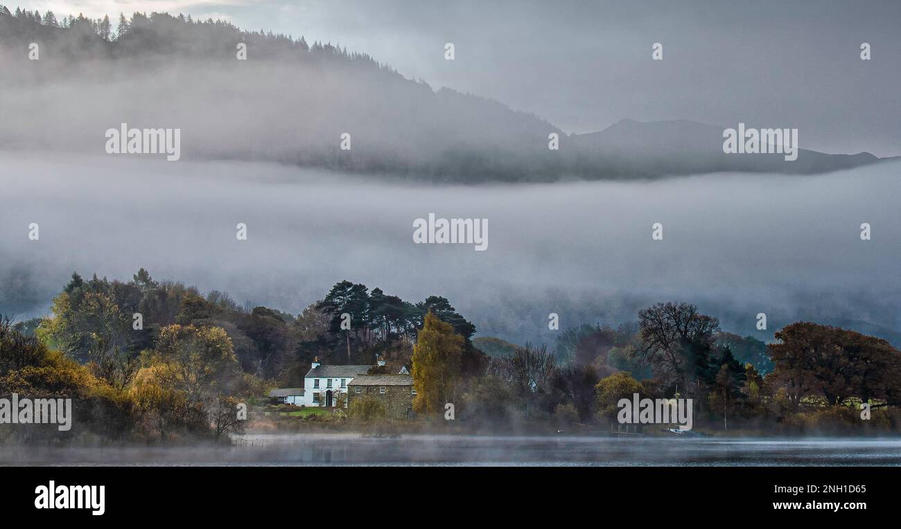 Nebbia seduta attraverso le campane sopra una fattoria sul lago all'alba Foto Stock