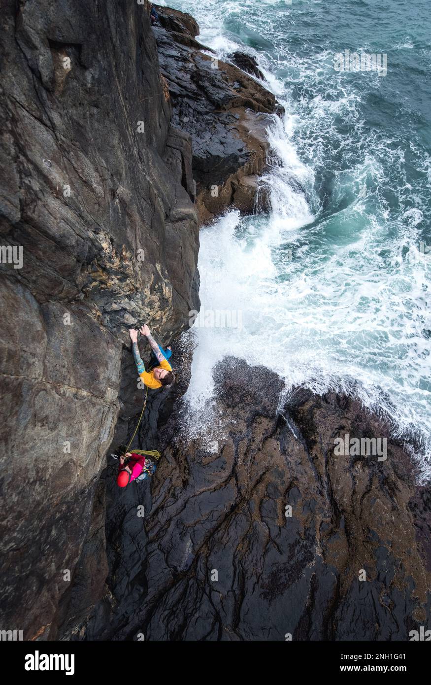 Uomo arrampicata su roccia sulla scogliera del mare con le onde che si schiantano sotto Foto Stock