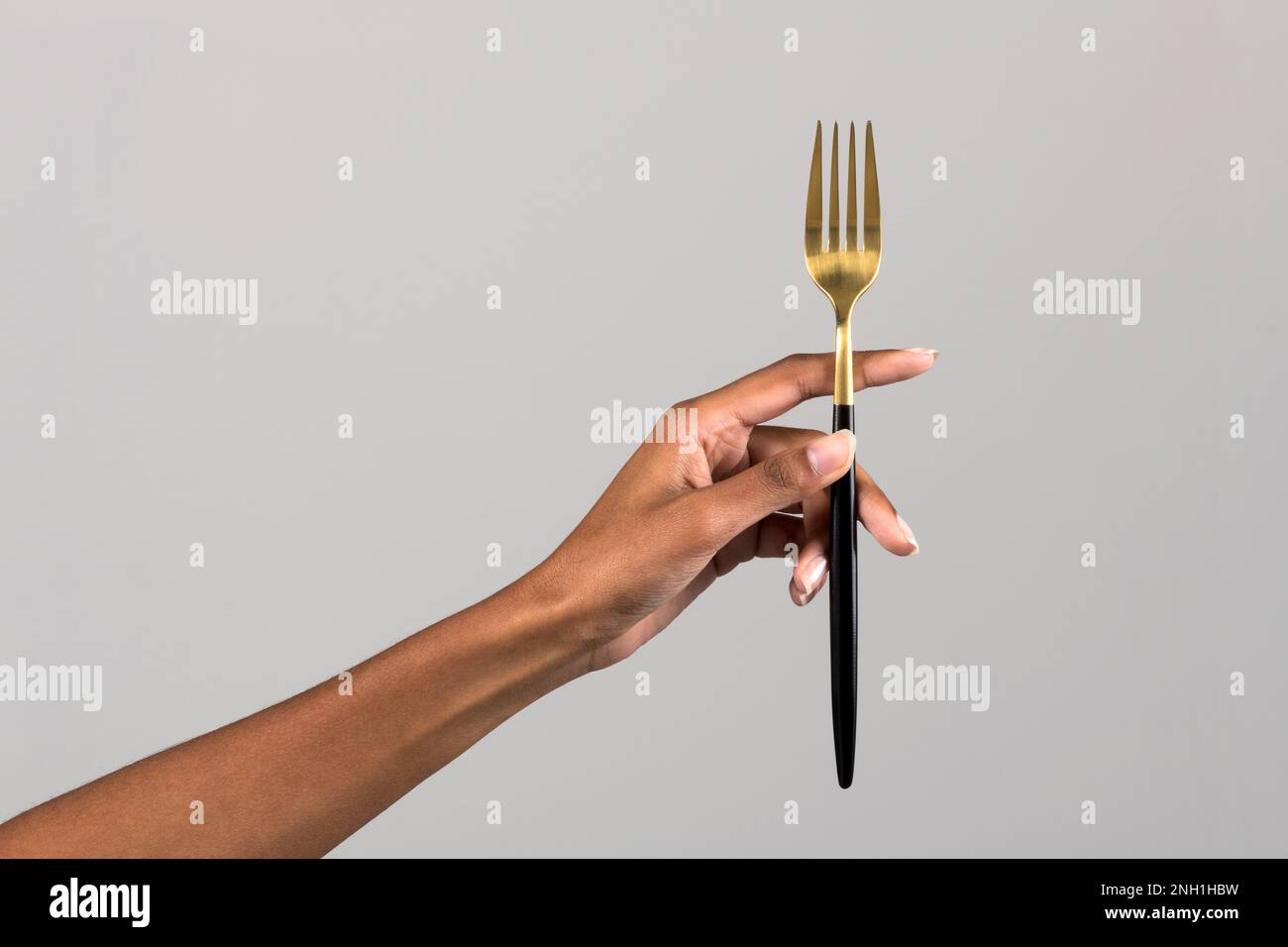 Crop anonima mano afro-americana femminile che mostra forcella nera e dorata isolata su sfondo grigio Foto Stock