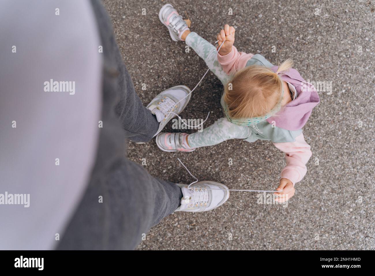 la bambina alla moda in un hooligan con cappuccio sciolge le scarpe del papà Foto Stock