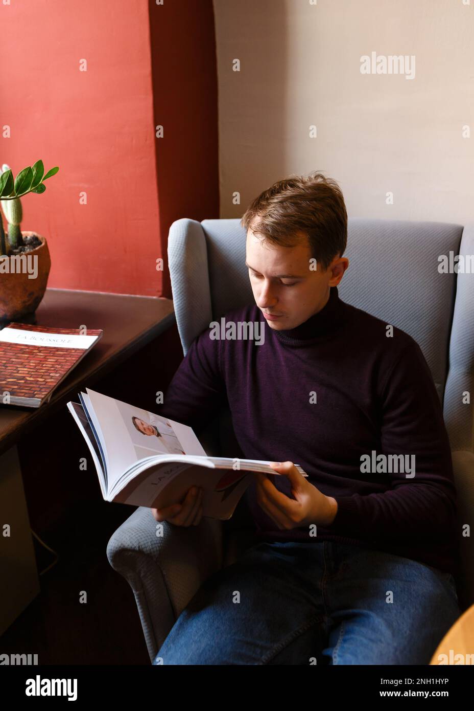 il giovane si siede da solo ad un tavolo con riviste Foto Stock