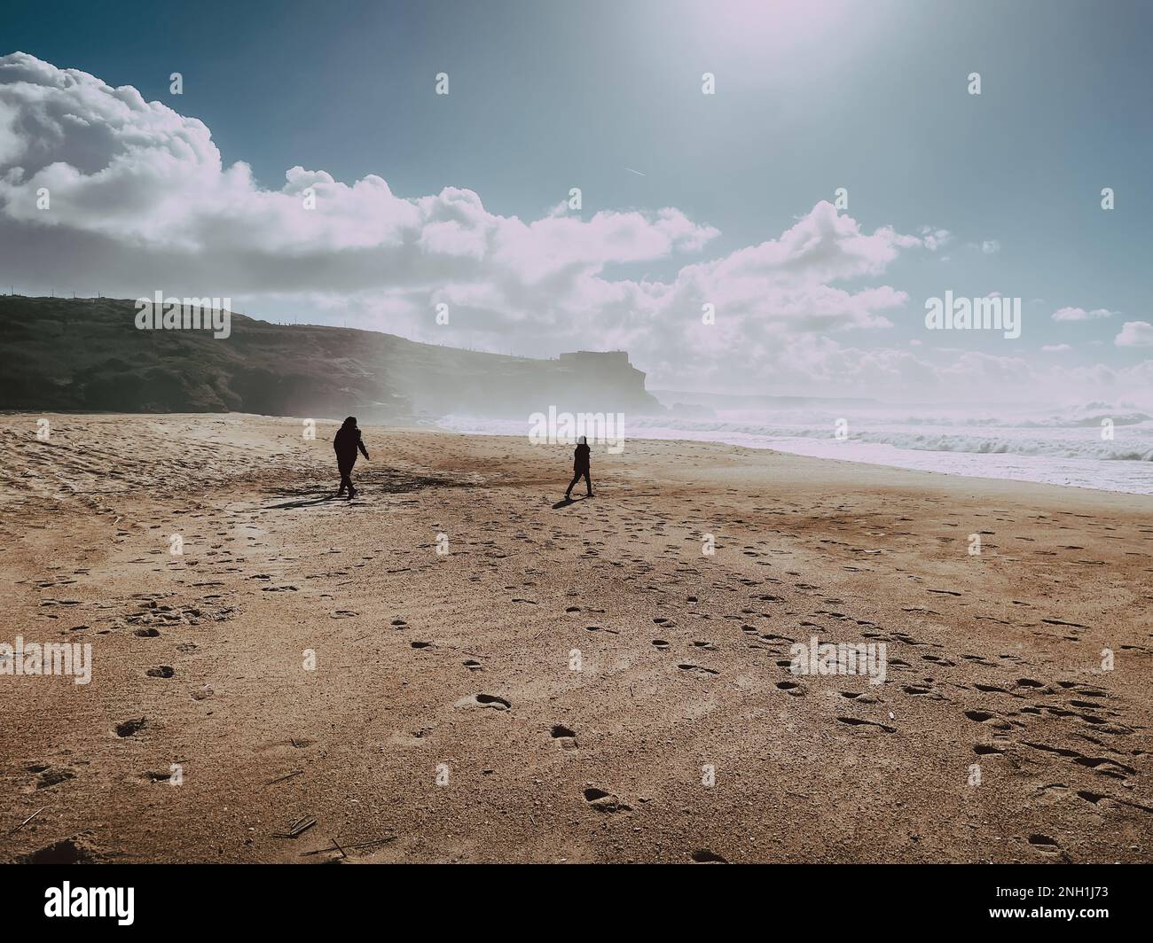 Persone silhouette scure su ampia spiaggia con scogliere a Nazare Foto Stock