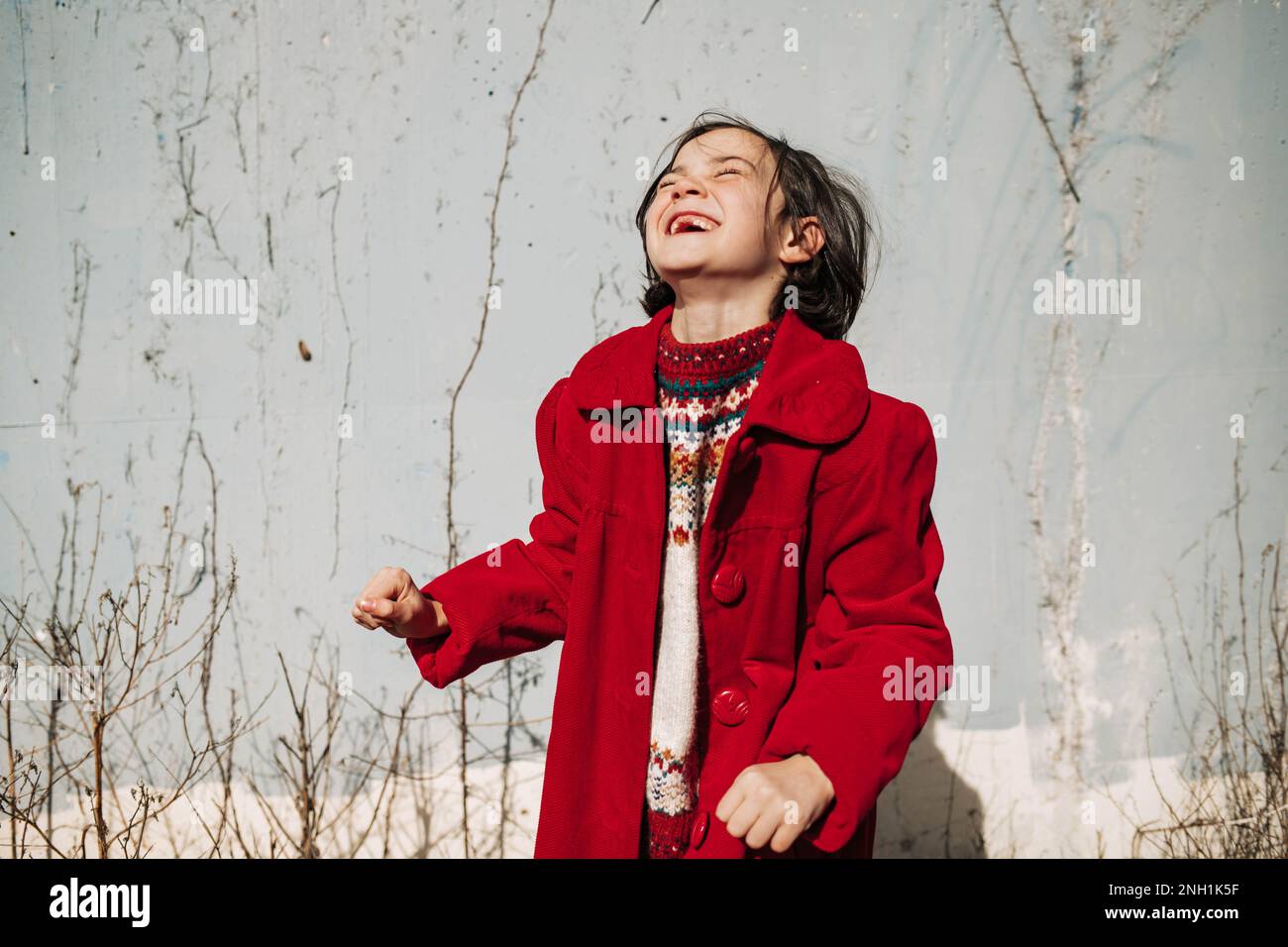ragazza in cappotto rosso ridendo di fronte al muro di cemento con viti Foto Stock