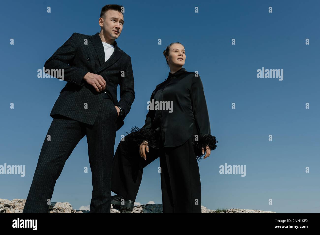 Un uomo e una ragazza in abiti neri stanno contro un cielo blu senza nuvole Foto Stock